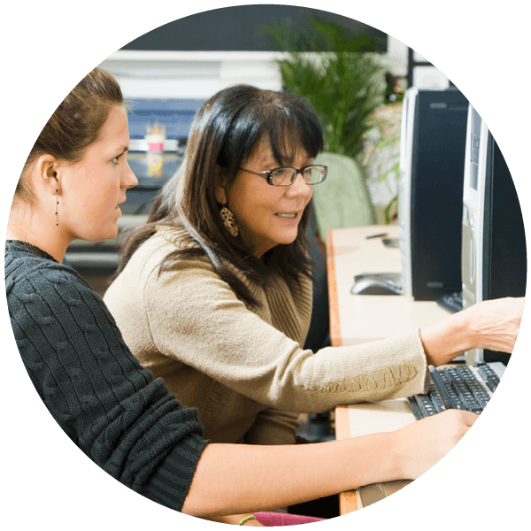 A student listens to a mentor as they work on a computer.